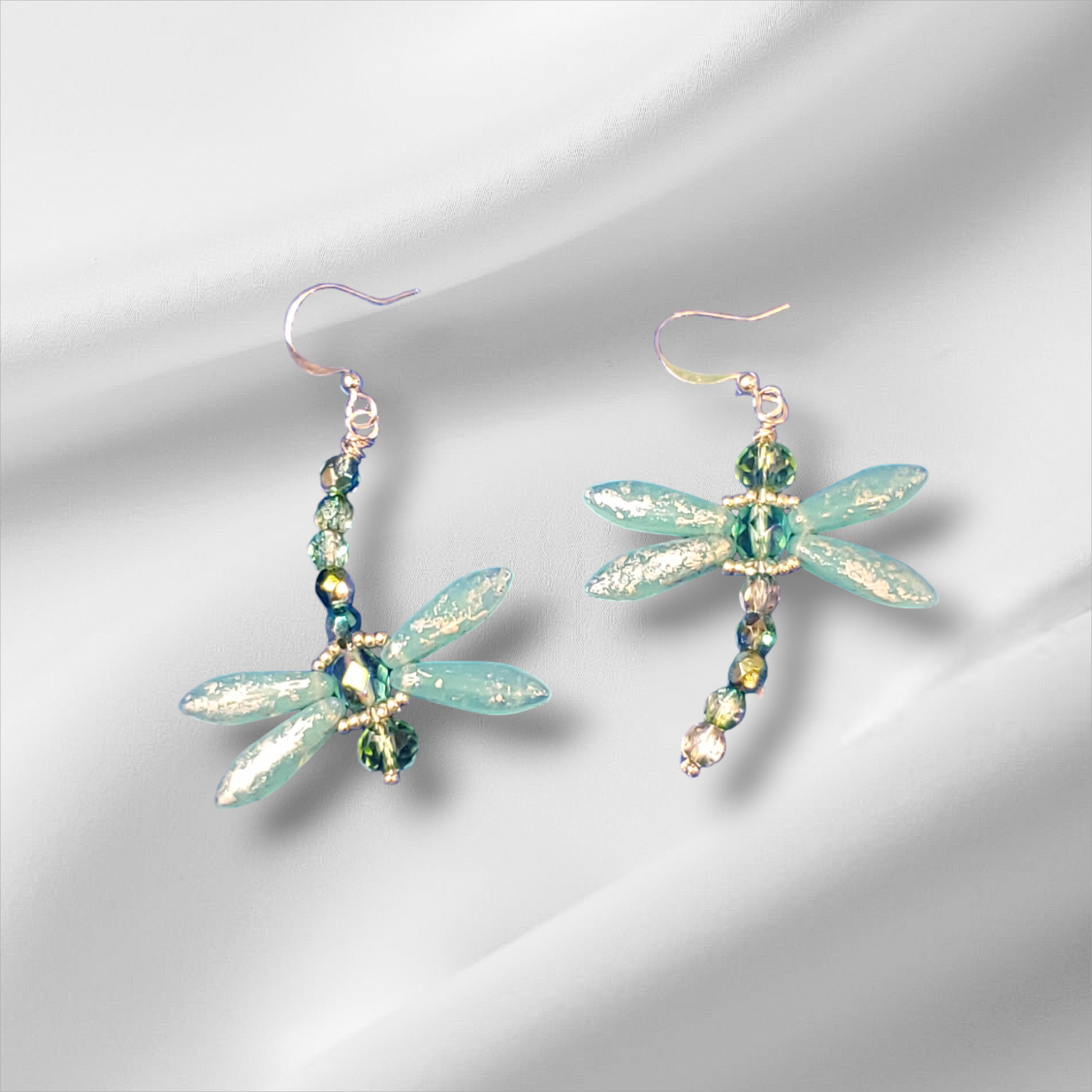 a pair of green dragonfly earrings on a white background