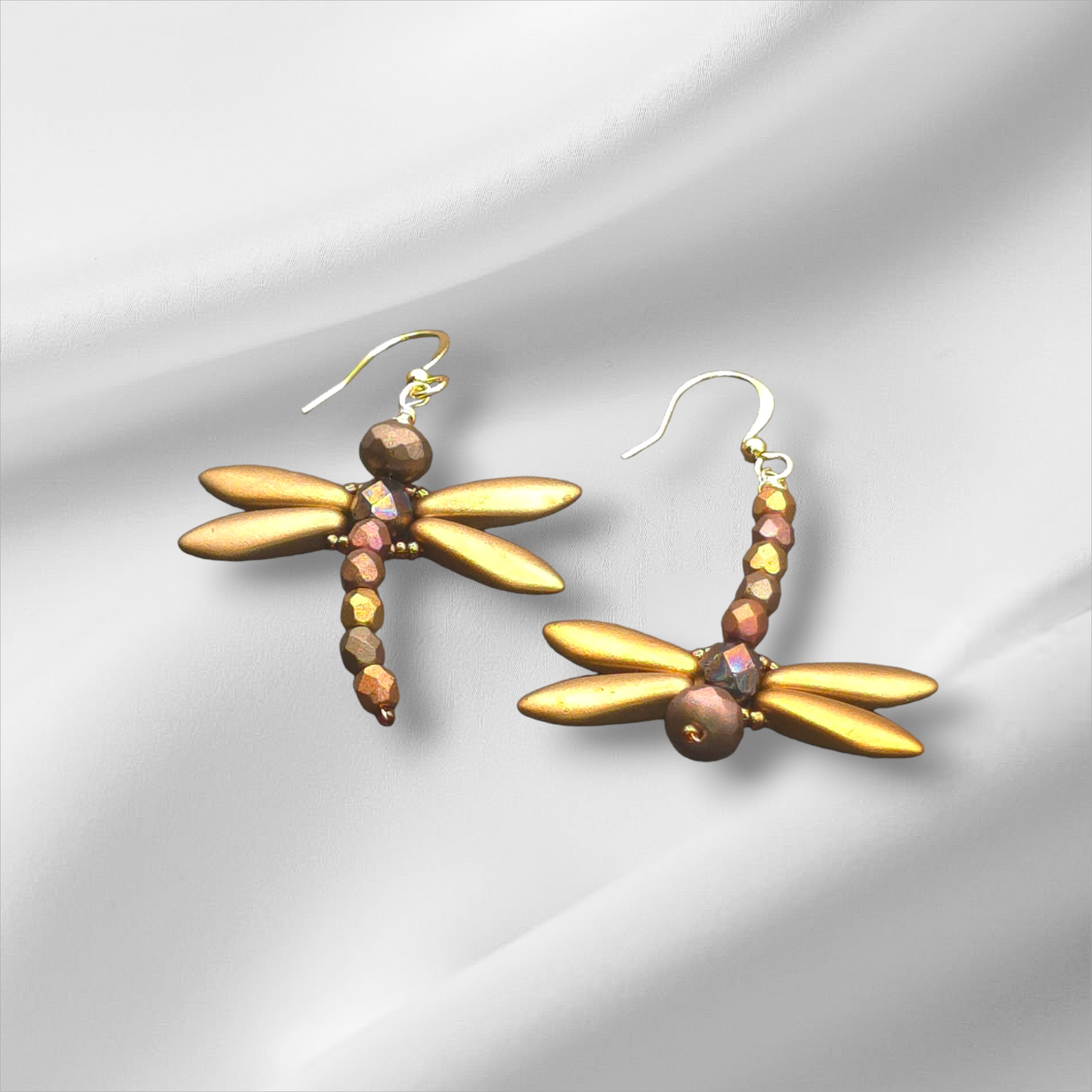 a pair of gold dragonfly earrings on a white background